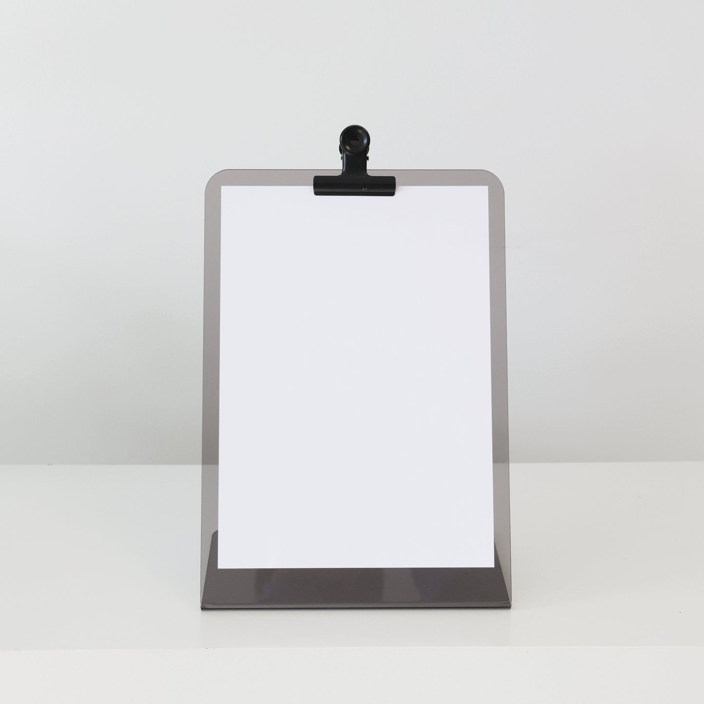 Présentoir en acrylique JOHN A4 équipé d’une pince noire, parfait pour menus ou programmes dans un espace d’accueil.